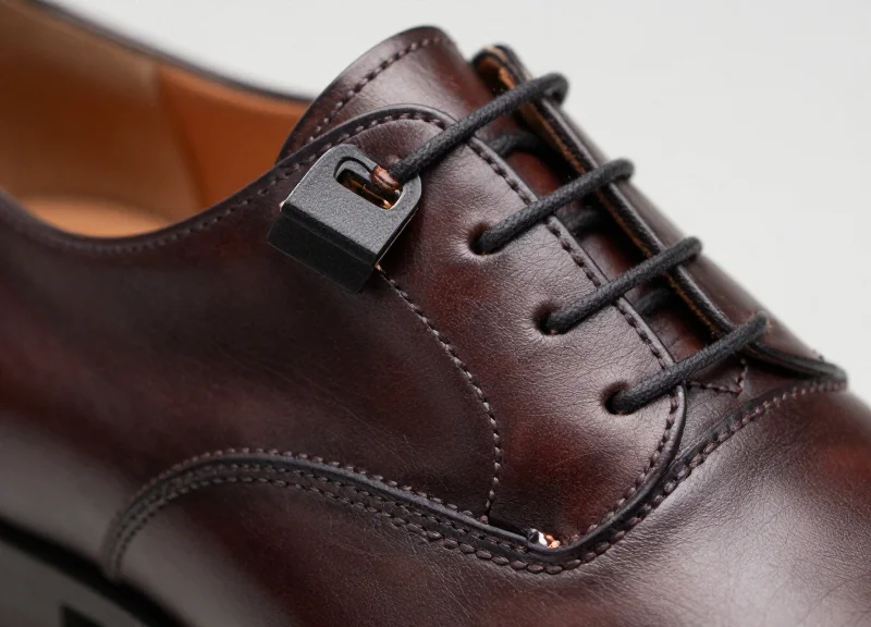 A close-up of a luxury leather shoe with a discreet security tag attached, showing the preserved material integrity.