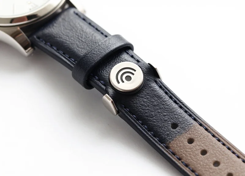 A luxury watch with a tiny, elegant RFID tag attached to its strap, shown against a clean background