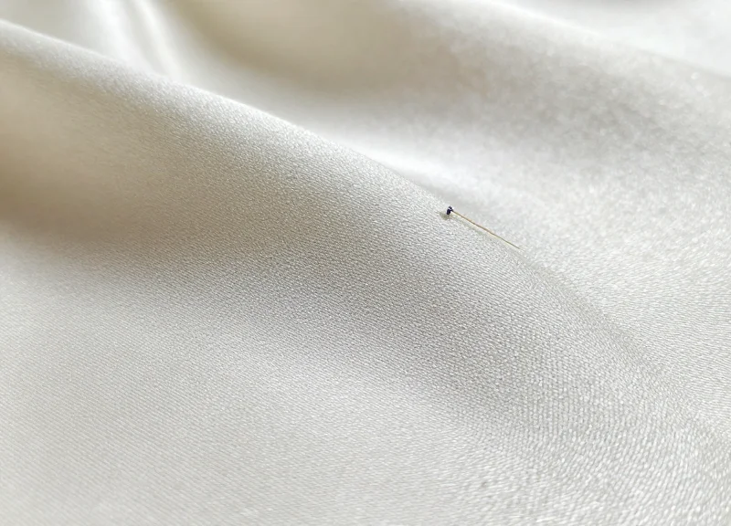 Macro photography of a security pin through fine silk fabric showing no damage.