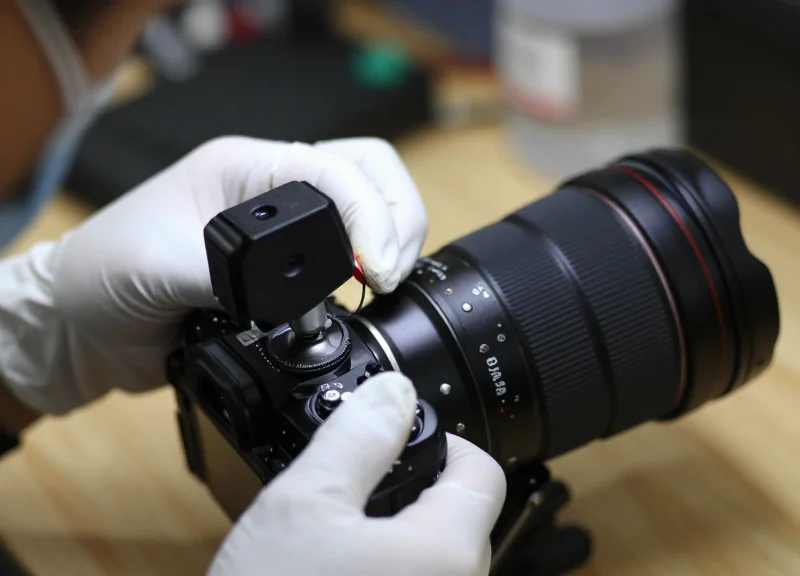 Technician hands installing a small sensor on a camera lens