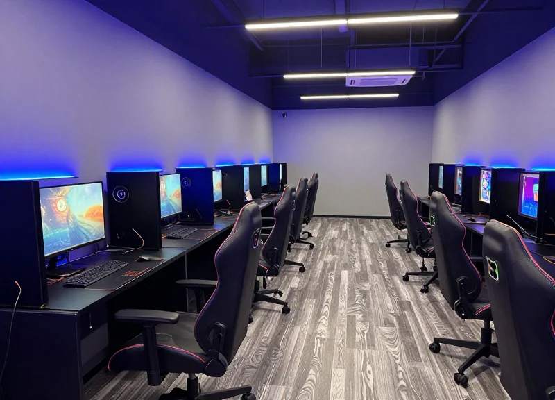 A high-end modern gaming lounge with ergonomic chairs, neon lighting, and rows of premium PCs.