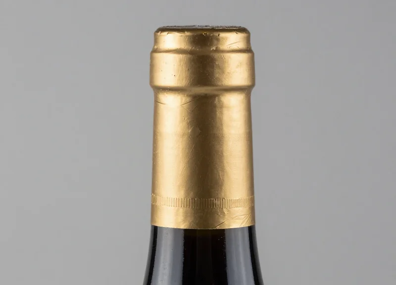 Macro close-up of a wine bottle neck wrapped in delicate gold foil with a neutral background.