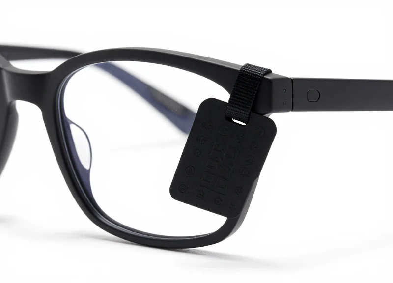A close-up of a specialized security tag attached to the temple of a pair of designer glasses