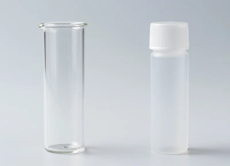 Side-by-side comparison of a glass lab vial and a polypropylene plastic vial in a laboratory rack.