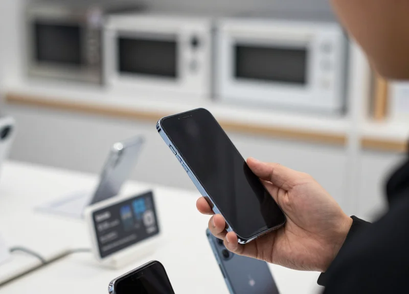 A customer holding a smartphone near an electronic shelf label in a modern store, demonstrating QR code interaction.