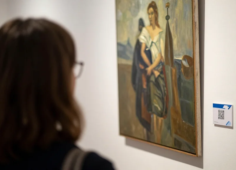 A visitor in an art gallery looking at an artwork while a digital label displays information nearby.